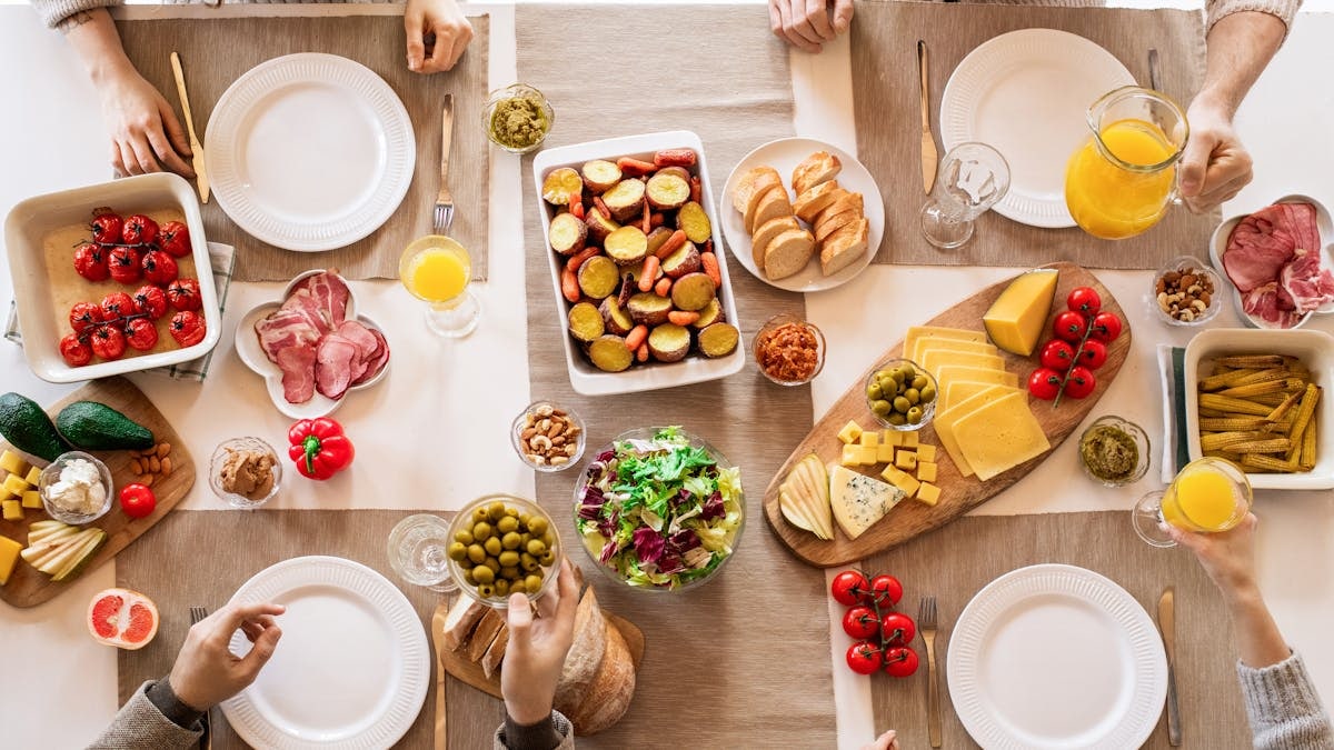 Overhead view of a lively brunch setup with assorted foods, cheeses, and juices on a table.